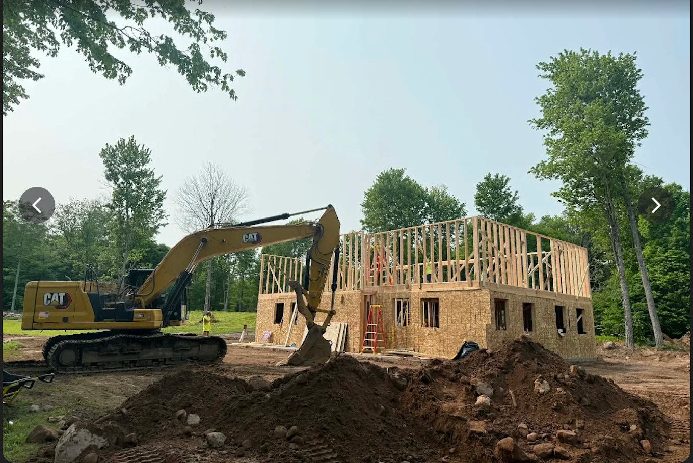 Excavator and topsoil piles around a new house under construction